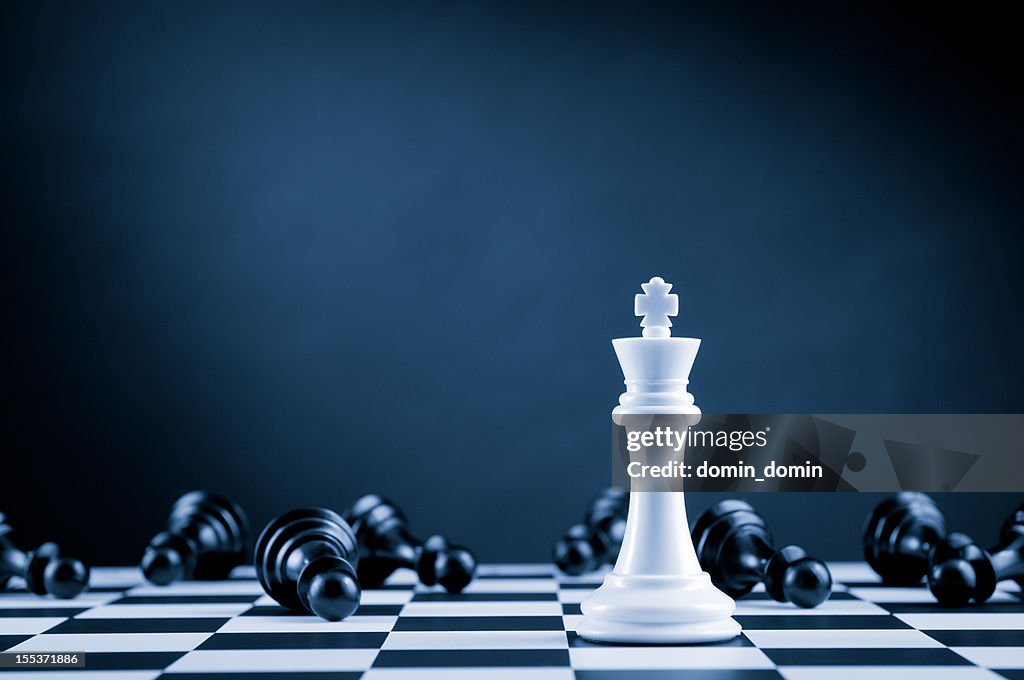 White Chess King among lying down black pawns on chessboard