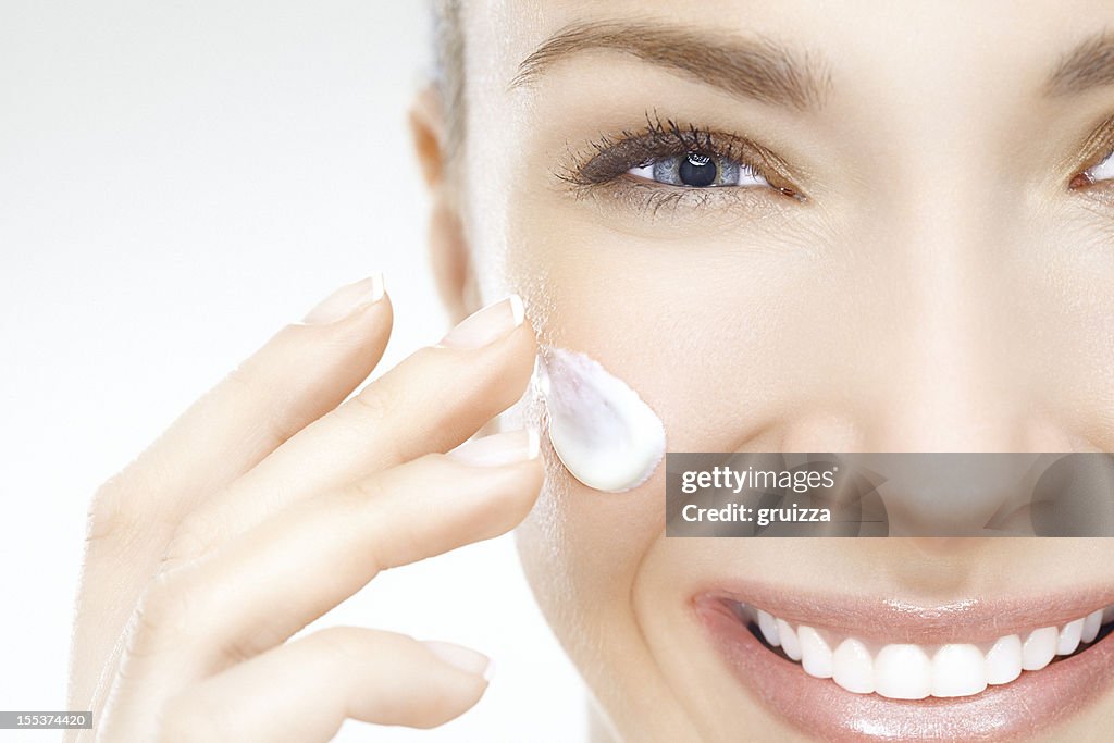 Close-up of a beautiful woman applying cream on her face