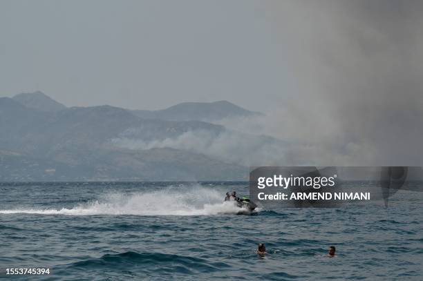 Beachgoers swim near the coastal town of Saranda as smoke billows from the Greek Island of Corfu on July 25, 2023. Authorities evacuated nearly 2,500...