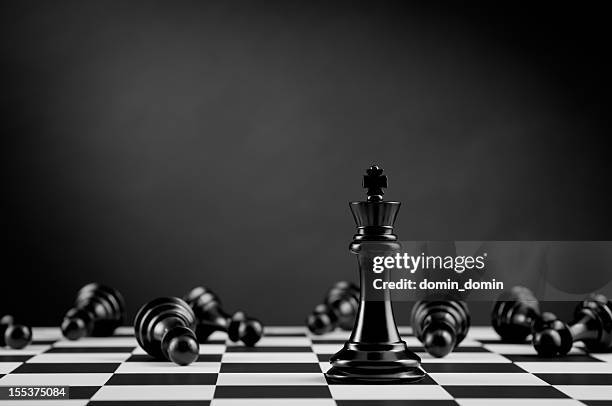 black chess king among lying pawns on chessboard - chess defeat stock pictures, royalty-free photos & images