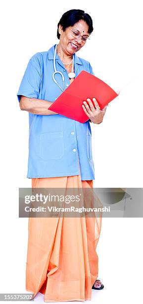 series... one cheerful senior indian female doctor reading medical report - indian doctor looking at camera stock pictures, royalty-free photos & images