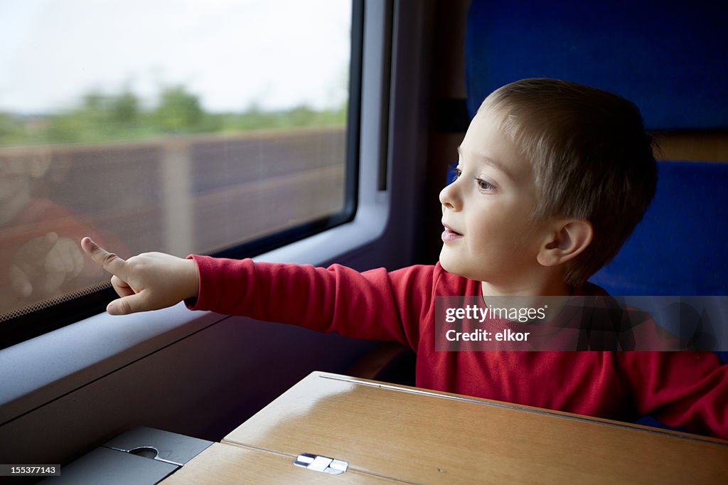 Three years old boy travelling in train pointing at window