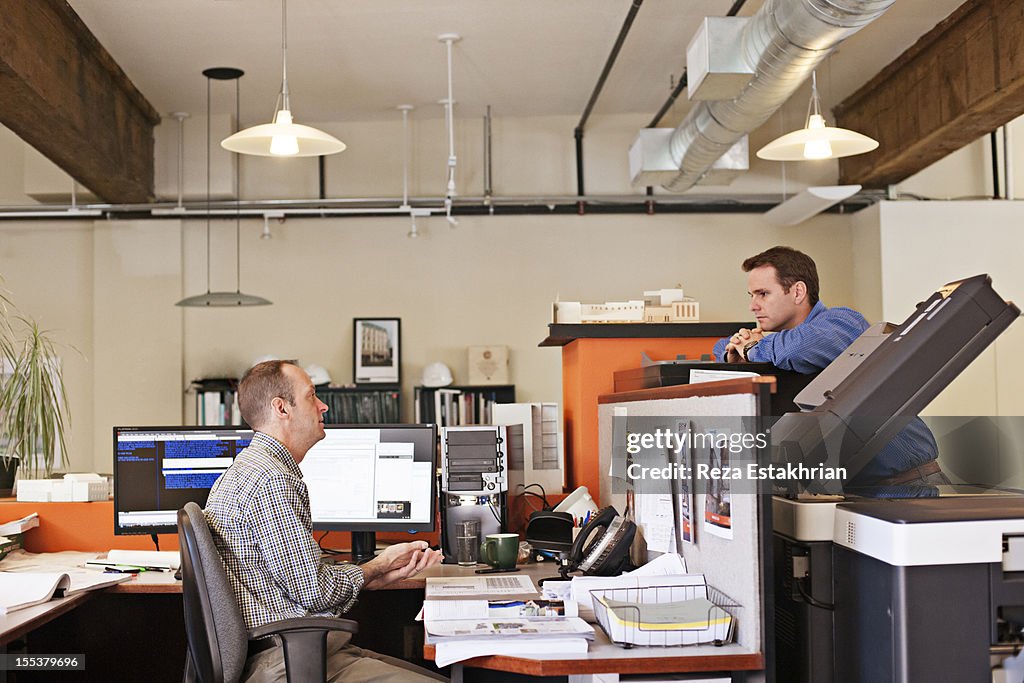 Two coworkers chat over office divide