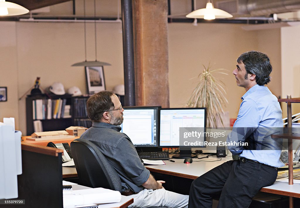 Two coworkers chat at desk