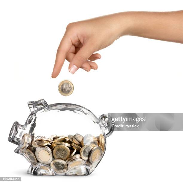 female hand dropping euro into half full piggy bank - euro in hand stock pictures, royalty-free photos & images