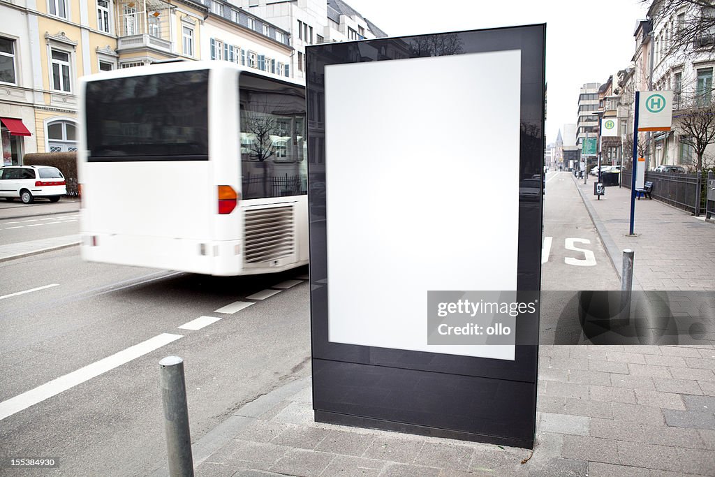 Blank advertising billboard on city street, bus passes