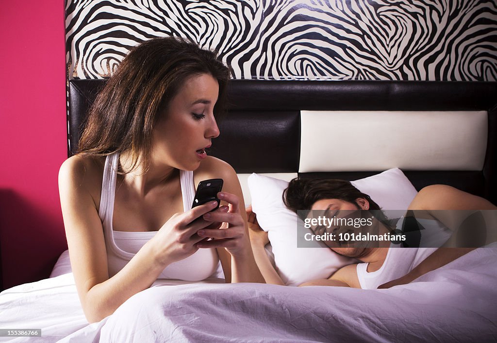 Woman on looking at mobile phone while her partner sleeps