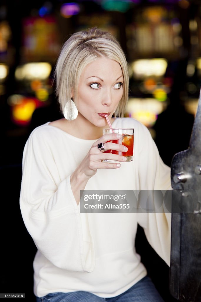 Young woman drinking cocktail at the slot machine