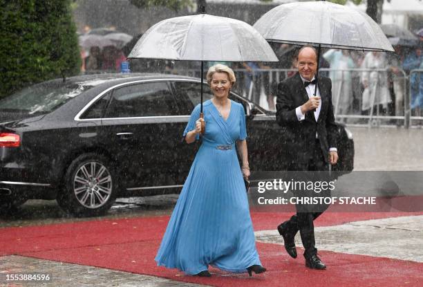 President of the European Commission Ursula von der Leyen and her husband Heiko von der Leyen arrive on the red carpet and hide under umbrellas to...