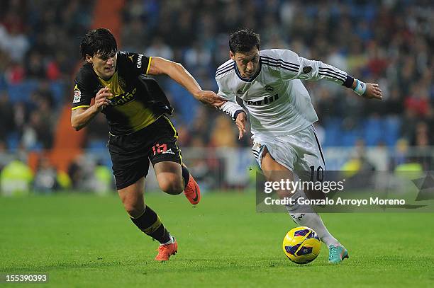 Mezut Ozil of Real Madrid CF competes for the ball with Cristian Sapunaru of Real Zaragoza during the La Liga match between Real Madrid CF and Real...