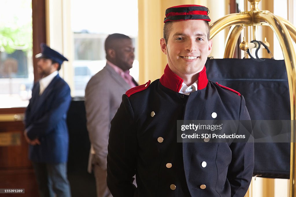 Bellhop standing in hotel lobby with guest's luggage on cart