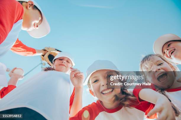 view from below of little league baseball players with hands in huddle, blue sky copy space - baseball huddle stock pictures, royalty-free photos & images