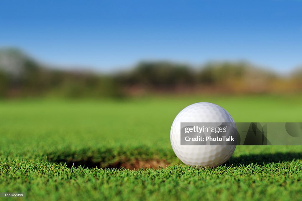 Ground level close up of golf ball close to hole