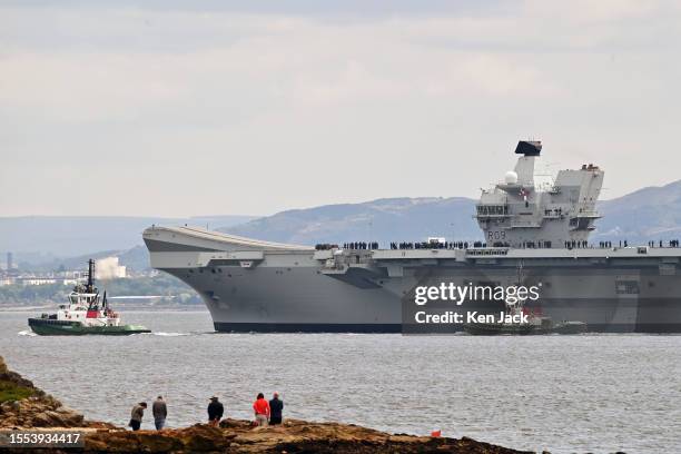 People watch from the shore as Royal Navy aircraft carrier HMS Prince of Wales is under way in the Firth of Forth with the Edinburgh skyline in the...