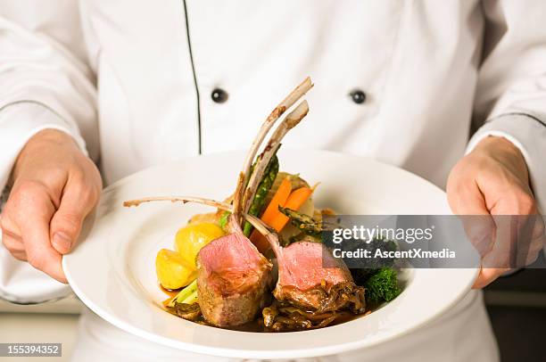 a freshly made rack of lamb being held by a chef  - hoofdgerecht stockfoto's en -beelden