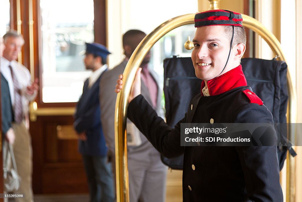 Bellhop holding luggage cart while waiting for hotel guests