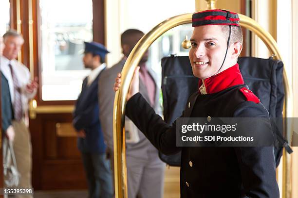 bellhop holding luggage cart while waiting for hotel guests - bell boy stock pictures, royalty-free photos & images