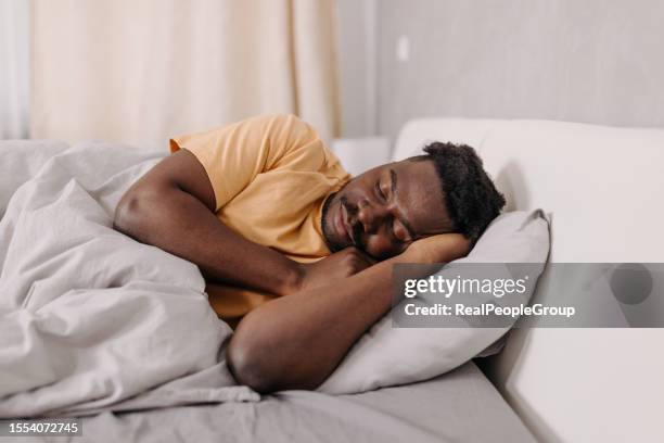 young man of african american descent finds tranquility and restfulness in his morning slumber - black man sleeping in bed stock pictures, royalty-free photos & images