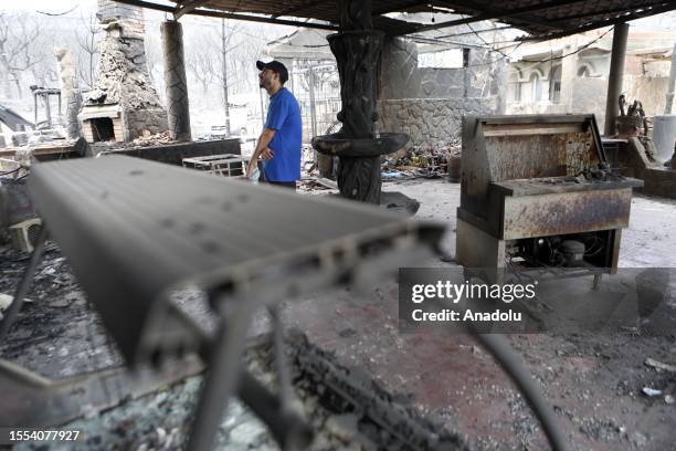 Man inspects the inside of a burned building as deadly wildfires ravage settlements along the country's Mediterranean coast and firefighters continue...