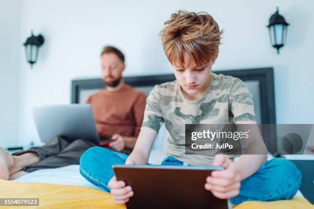 father working from home using laptop with his son using digital tablet nearby - lifehack stock pictures, royalty-free photos & images