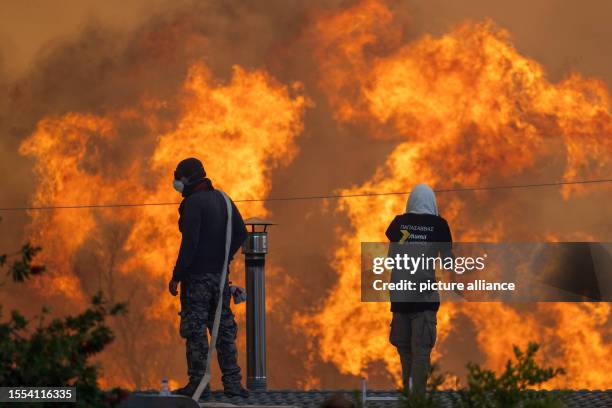 Dpatop - 25 July 2023, Greece, Gennadi: Towards evening flames reach the village of Gennadi, residents stand on their roofs in front of huge flames...