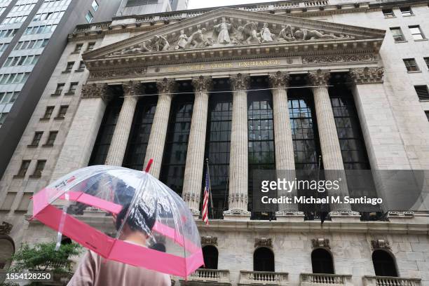 Person stands under an umbrella outside of the New York Stock Exchange during afternoon trading on July 18, 2023 in New York City. Stocks closed...