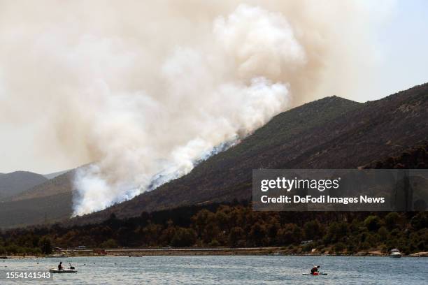 Tourists on the beach watch as an airplane refuels it's water tank with water as it waterbombs a local fire nearby, in Grebastica, Croatia in July...