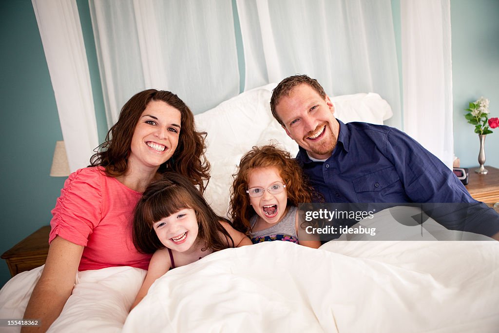 Happy Sisters Cuddling With Dad and Mom in Bedroom