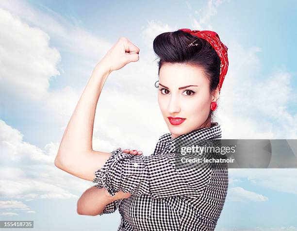 brunette striking a famous rosie riveter pose - rolling up sleeve stock pictures, royalty-free photos & images