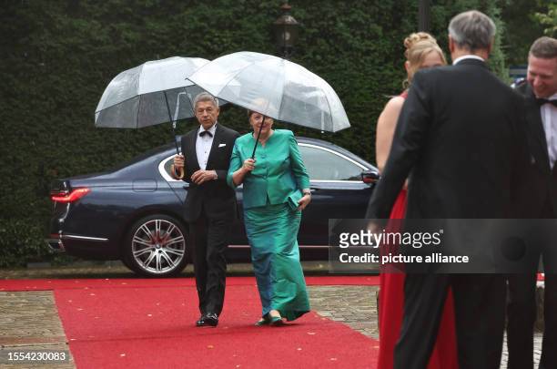 July 2023, Bavaria, Bayreuth: Former German Chancellor Angela Merkel and husband Joachim Sauer arrive with umbrellas for the opening of the Richard...