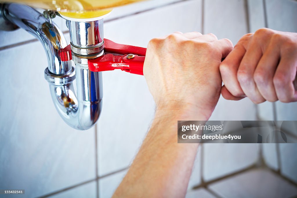 Plumber hands holding wrench and fixing a sink in bathroom