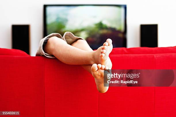 casual cross-legged boy plays on red couch - feet up tv stock pictures, royalty-free photos & images