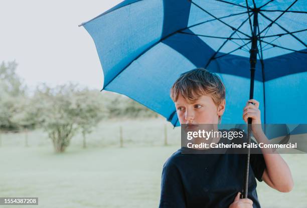 a little boy shelters under a large blue umbrella - boys taking a shower stock pictures, royalty-free photos & images