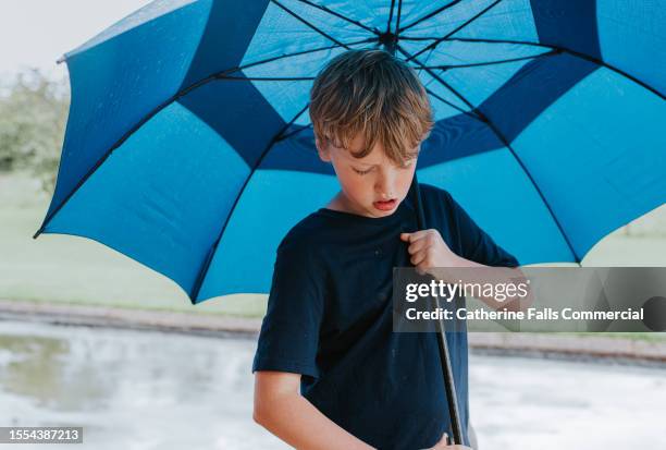 a little boy shelters under a large blue umbrella - boys taking a shower stock pictures, royalty-free photos & images