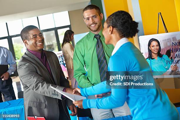 professional accepting resume application from businesswoman at job fair - job fair stock pictures, royalty-free photos & images