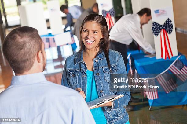 happy volunteer asking exit poll questions at election voting center - local politics stockfoto's en -beelden