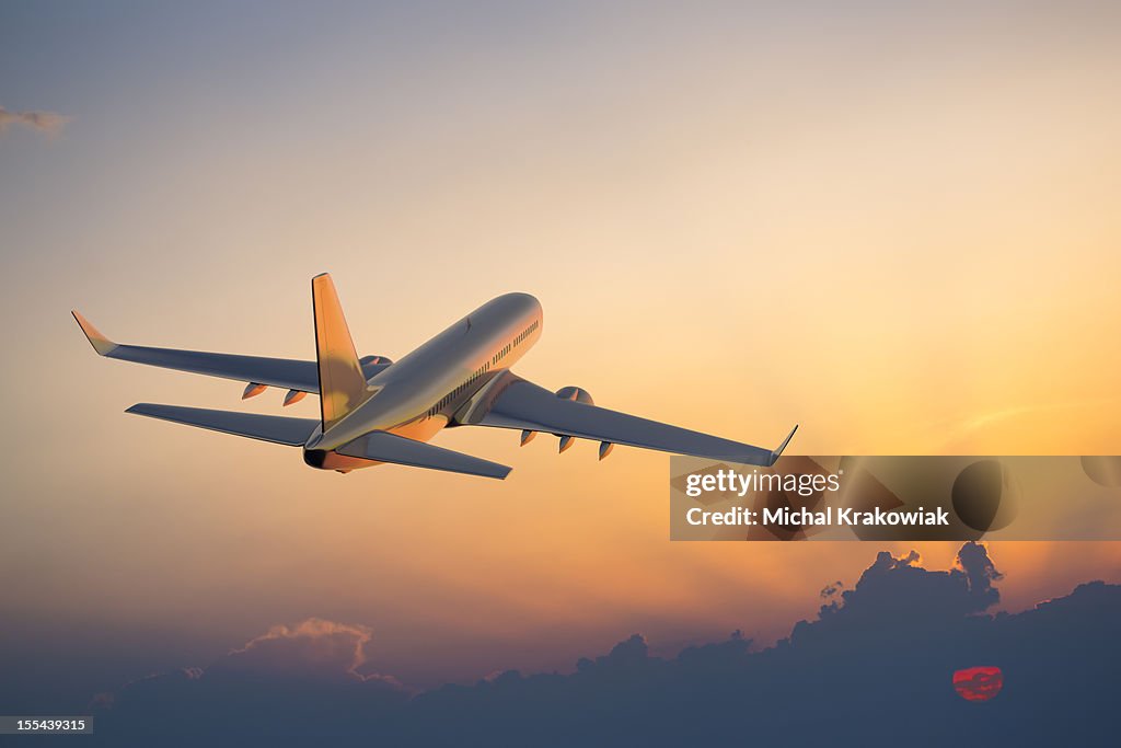 Passenger airplane flying above clouds during sunset