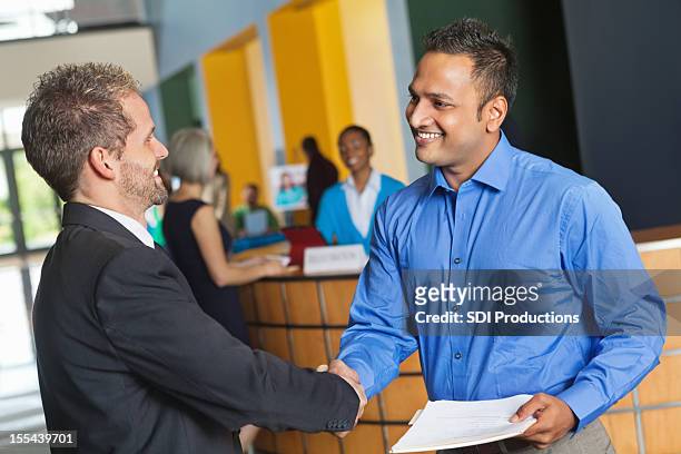 two business men shaking hands exchanging resumes at job fair - job fair stock pictures, royalty-free photos & images
