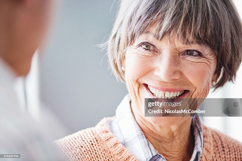 Primer plano de mujer senior sonriendo ampliamente en conversación