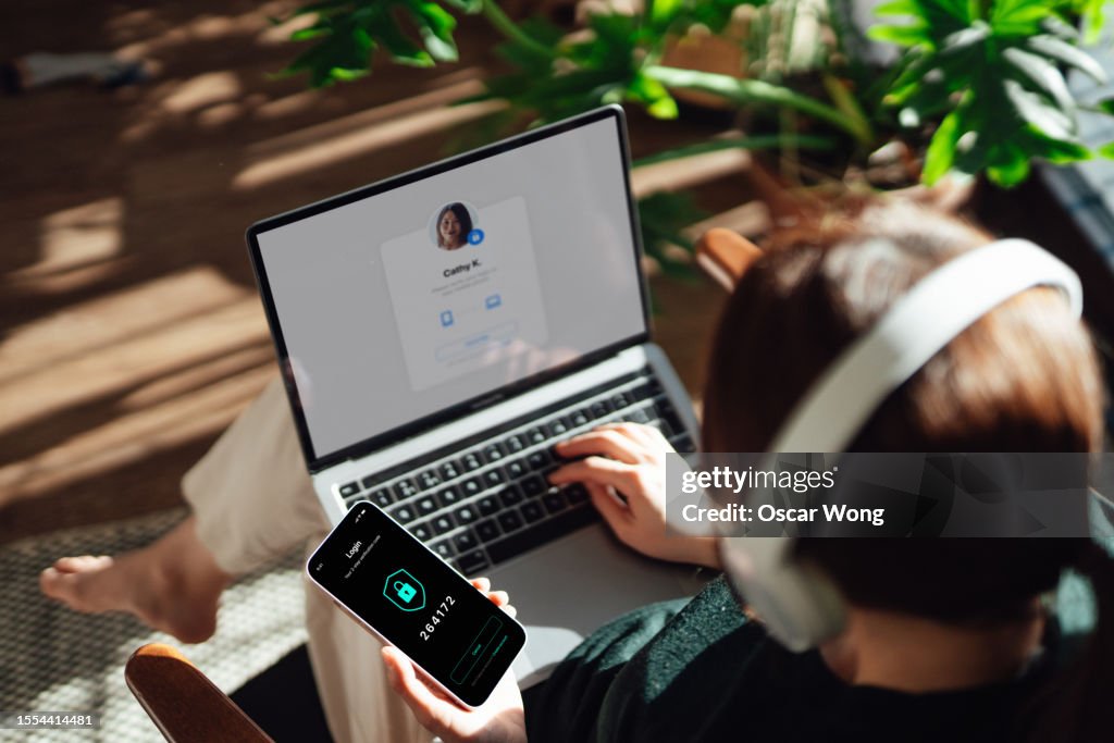 Over the shoulder view of young woman logging in online account with Two-Factor Authentication (2FA) security system visa smart phone and laptop