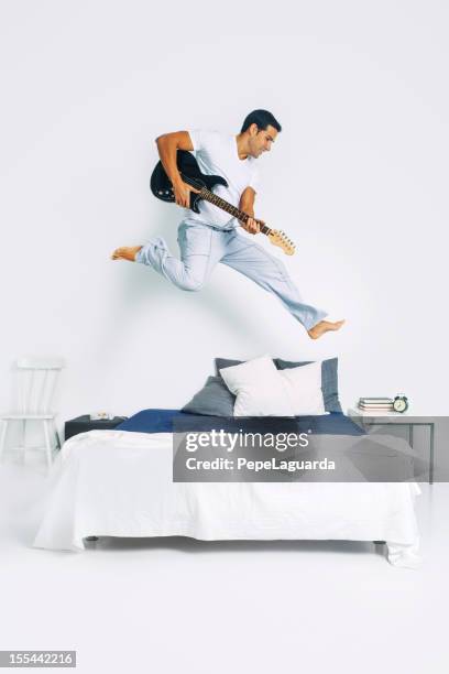 man jumping on bed playing electric guitar - jumping on bed stockfoto's en -beelden