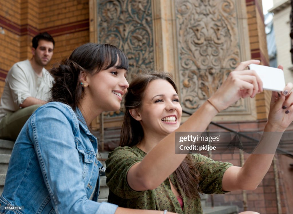 Smiling young women taking picture with smart phone