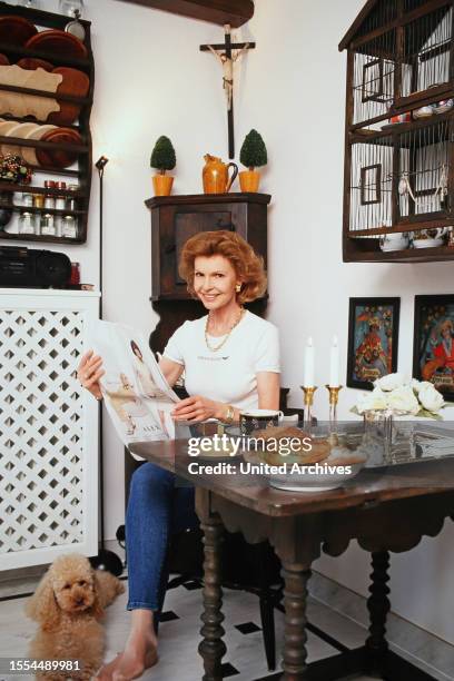 Jutta Kammann, deutsche Schauspielerin, bei einem Homestory Fotoshooting mit Tageszeitung und ihrem Pudel in ihrer Küche in München, Deutschland 1999.