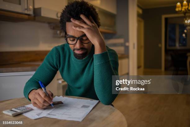 young man using calculator while going through bills and home finances - debt stock pictures, royalty-free photos & images