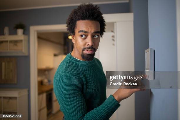 young man adjusts the temperature at home with a device on the wall - lock sporting position stock pictures, royalty-free photos & images