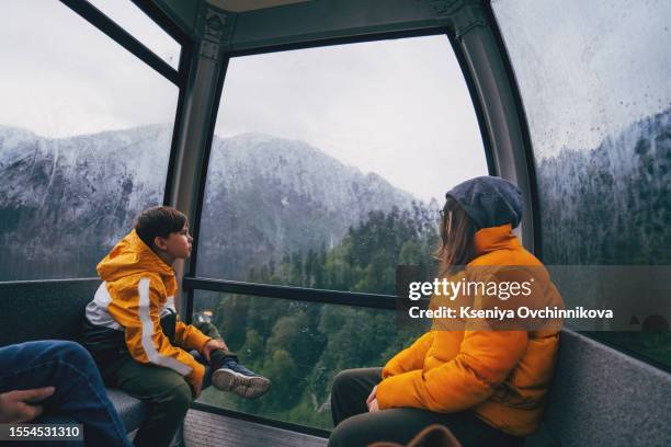 an attractive blonde model sits in a cable car cabin and admires the view. beautiful woman climbs the funicular in the mountains in autumn - majestic hotel stock pictures, royalty-free photos & images