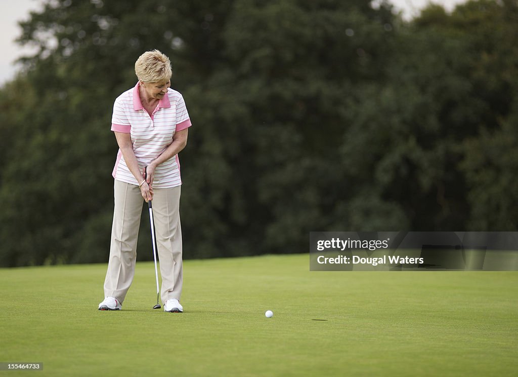 Female golfer putting ball towards hole.