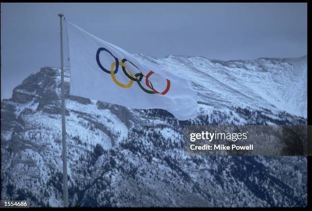 THE OLYMPIC FLAG BLOWS IN THE STRONG WINDS OF CANADA IN FRONT OF AN IMPRESSIVE BACKDROP OF SNOWY MOUNTAIN TOPS DURING THE 1988 WINTER OLYMPICS HELD...