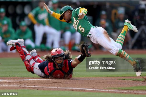 Tony Kemp of the Oakland Athletics jumps over Jorge Alfaro of the Boston Red Sox to try to score on a wild pitch in the first inning at RingCentral...