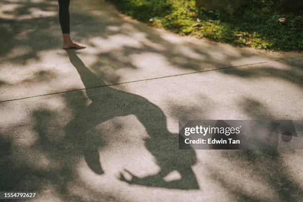 schatten einer asiatischen chinesischen frau, die am wochenendmorgen im öffentlichen park yoga praktiziert - schatten im mittelpunkt stock-fotos und bilder